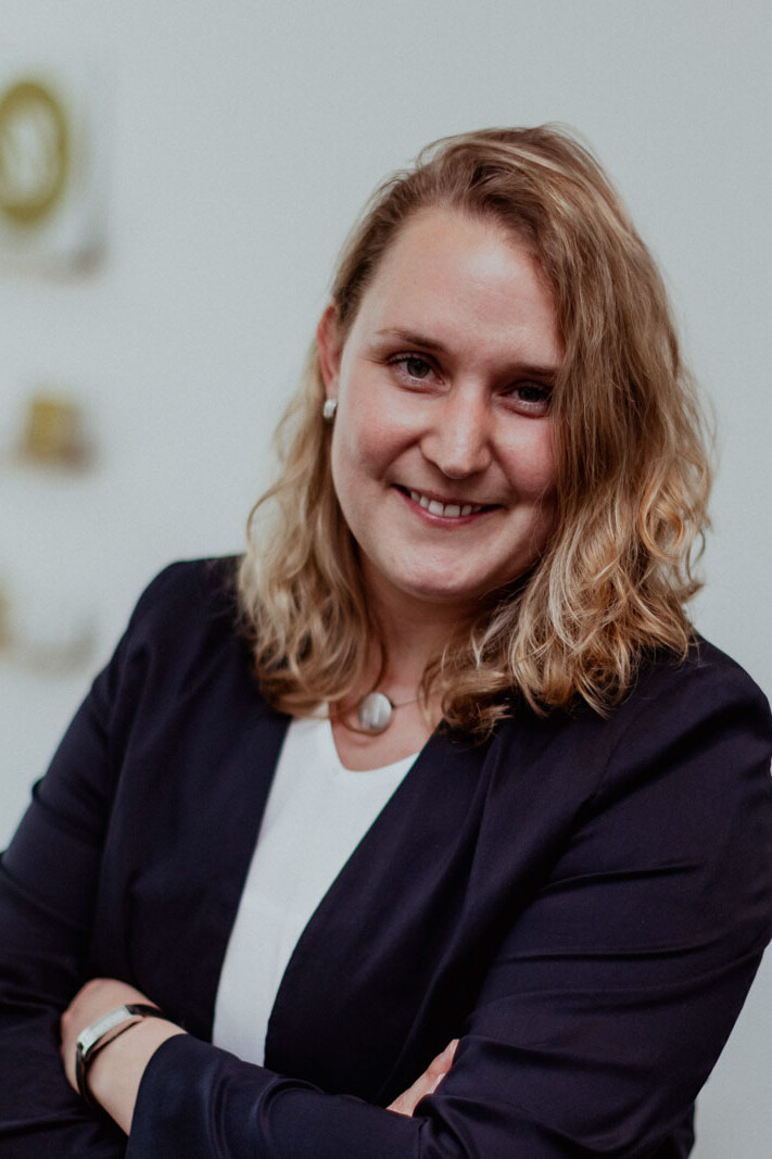 Rechtsanw&auml;ltin Frau Beckmann mit verschr&auml;nkten Armen vor der Visitenkartenwand